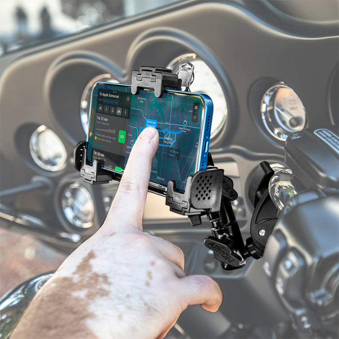 A hand touches a smartphone with a GPS map on a motorcycle dashboard, secured by the LockVise™ Universal Locking Phone Holder with Multi-Angle and Clamp Mount. Speedometers and control dials are visible in the background.