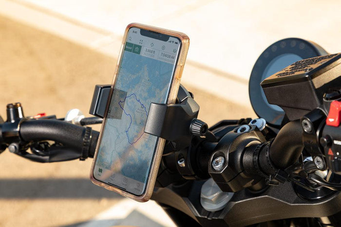 A smartphone with a map is held by the RoadVise® Ultra Holder with Aluminum Handlebar Mount on motorcycle handlebars for safe navigation. The photo is taken outdoors in daylight.