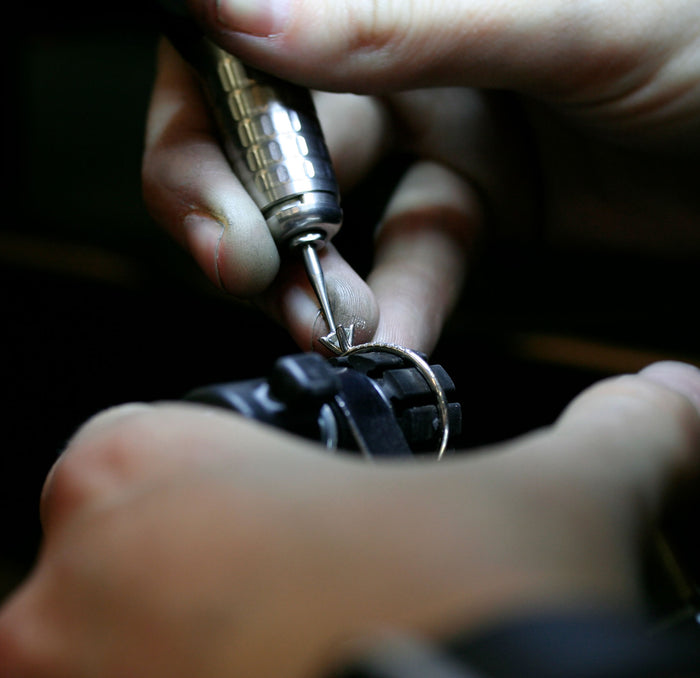 Guldsmed som infattar en diamant i en ring med ett fattar verktyg.