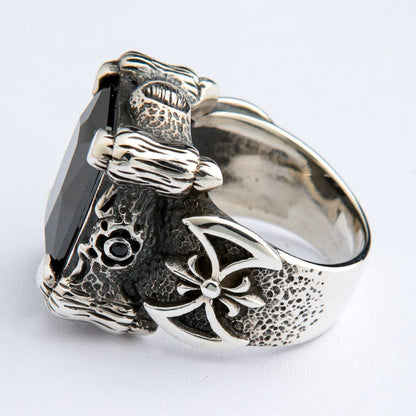 Four claw prongs grip the faceted black stone, with a raised cross motif set into the textured band.