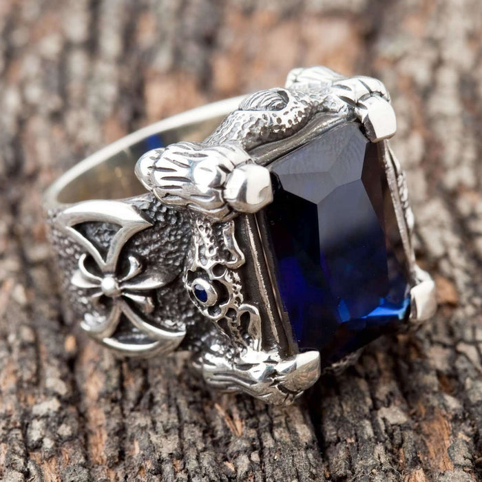 A close-up of the silver dragon talon ring, detailing the four powerful claws gripping the large blue stone.