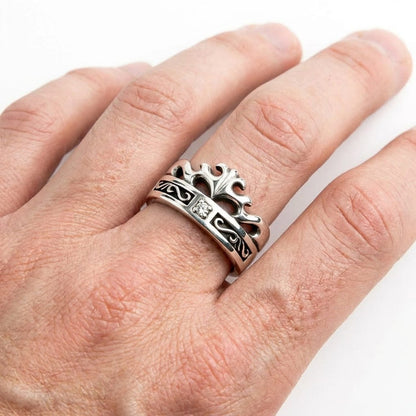 Close-up of a sterling silver Celtic crown band ring featuring oxidized swirl details and a small clear center stone, worn on a man's hand against a white background.