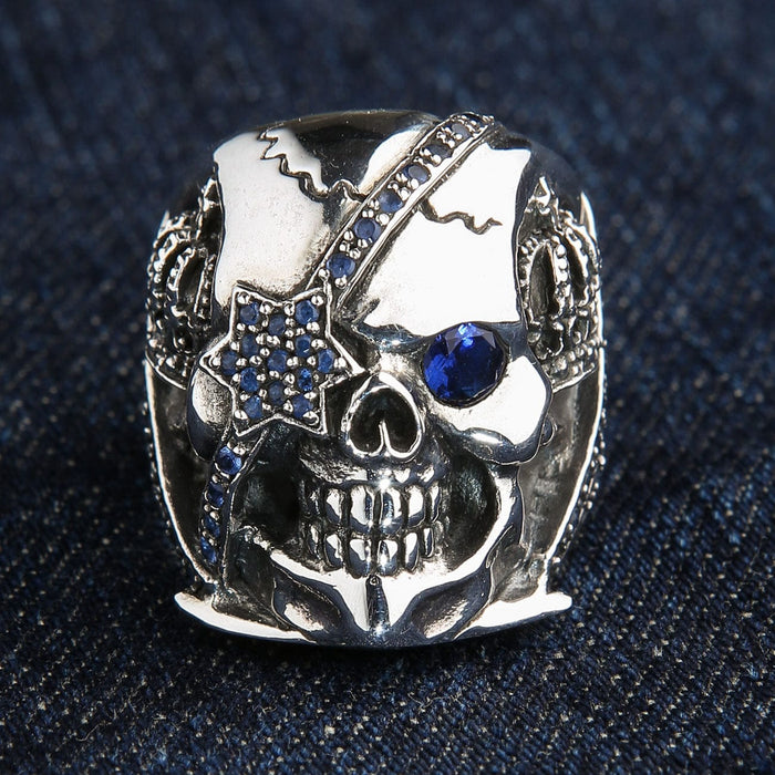 The blue eye patch skull ring displayed on a dark blue denim texture.