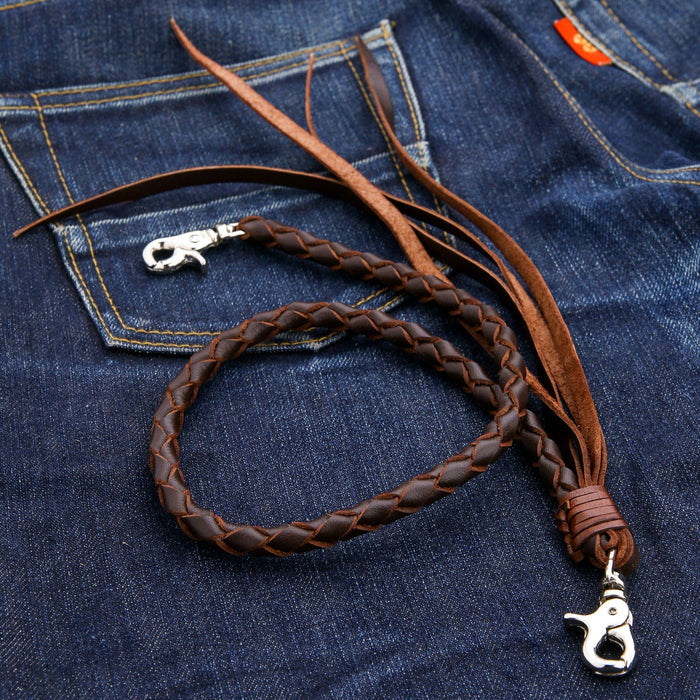 A dark brown braided leather wallet chain coiled on a jean's back pocket, highlighting the silver clasp and leather tassels.