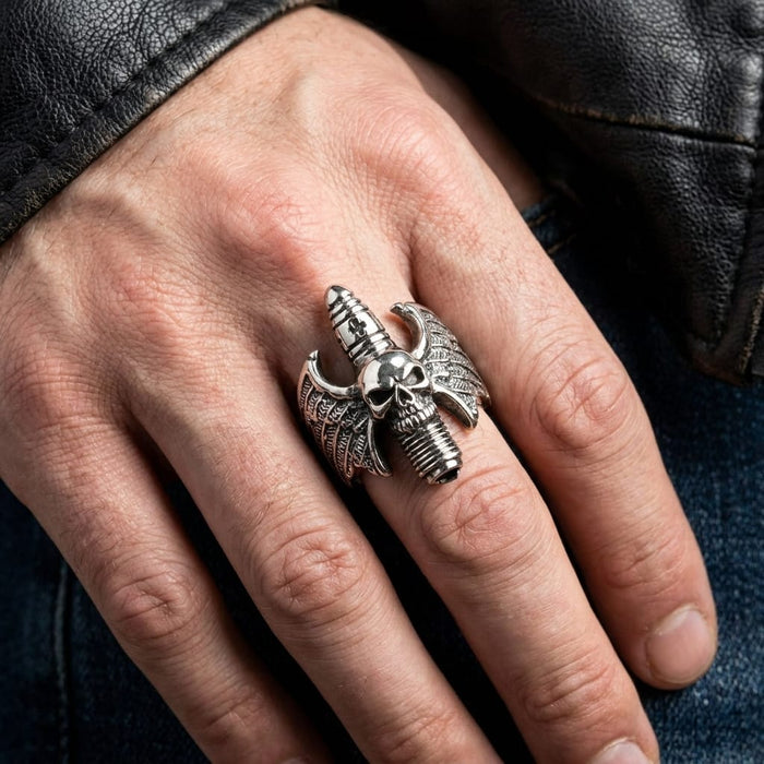 Close-up lifestyle shot of a man's hand wearing a detailed silver devil skull ring with wings, styled casually with a black leather jacket and blue jeans.