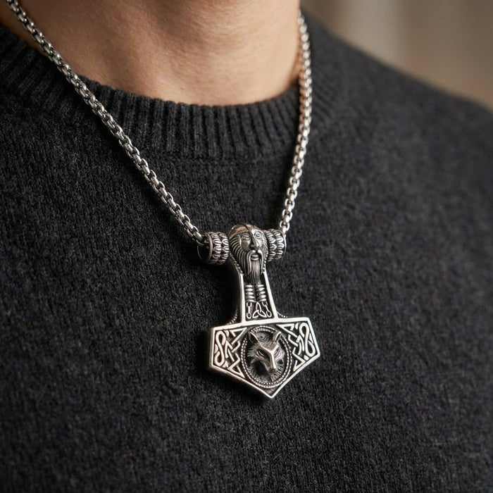 Close-up of the silver Norse hammer on a dark sweater, showcasing the central Fenrir wolf design and intricate knotwork.