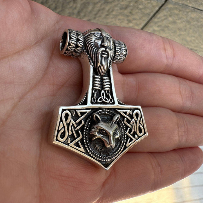 Resting on fingers, the front face of the .925 silver amulet displays Thor's carved beard, a triquetra, and Fenrir.