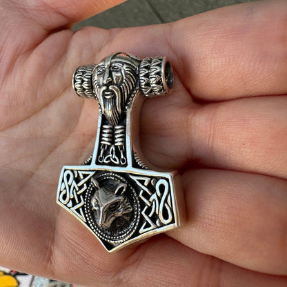 Angled view highlighting the thick silver edge and deep relief of the carved wolf and bearded face on the Mjolnir.