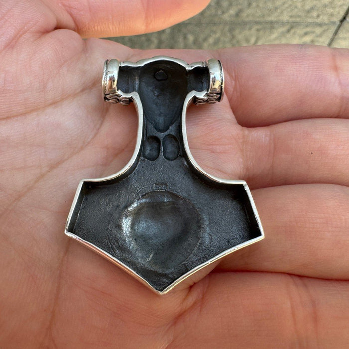 Reverse side of the silver Mjolnir in a palm, revealing the hollowed textured back and a central 925 hallmark stamp.