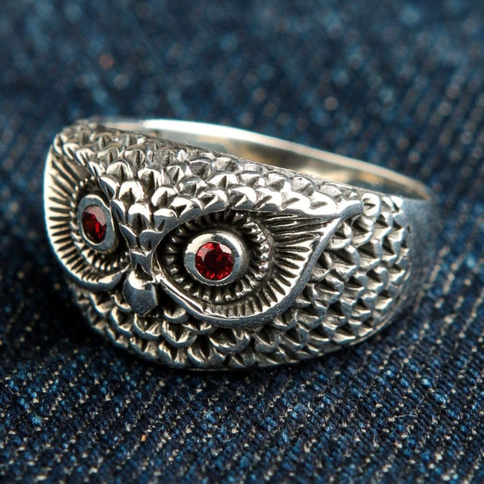 Three-quarter view of 925 sterling silver owl ring displaying oxidized feather details and red garnet eyes