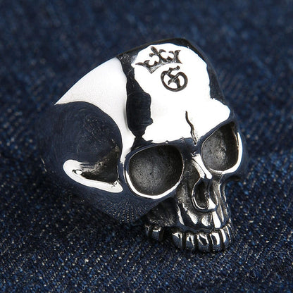 Macro top view of the solid silver skull ring on denim, emphasizing the high-polish forehead and distinct engraved symbols.