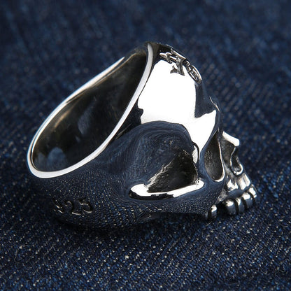Rear angled view of the heavy sterling silver skull ring resting on denim, revealing the thick band and exterior 925 stamp.
