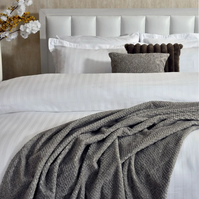 White pinstripe duvet cover with gray draped throw and brown bolster pillows