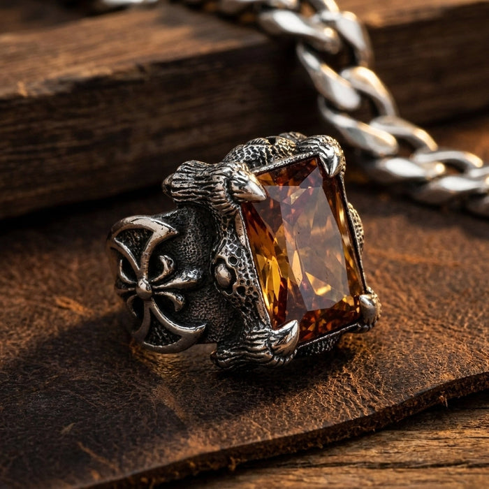 Imperial Topaz dragon claw ring resting on dark leather beside a silver curb chain in warm gothic lighting