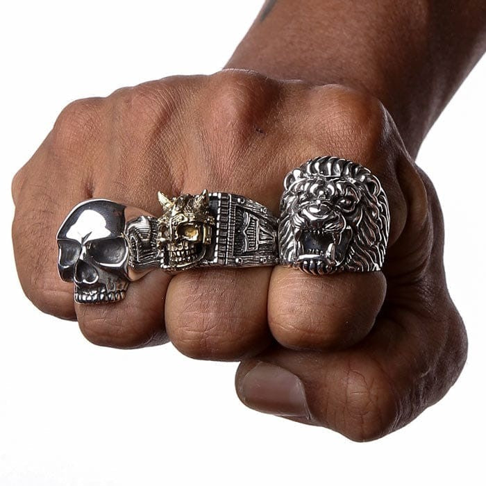 Clenched fist wearing the Keith Richards skull ring alongside a lion ring and ornate silver bands for a stacked biker look