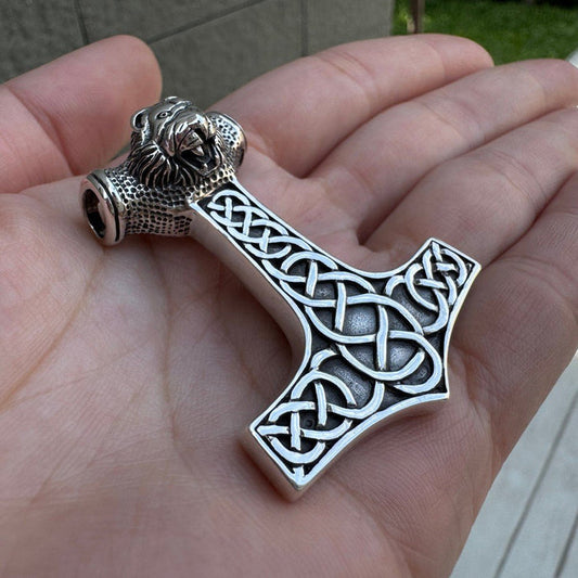 Silver Mjölnir pendant held in an open palm, showcasing intricate Celtic knotwork and a detailed roaring lion head.