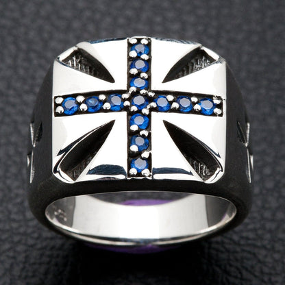 A solid sterling silver Maltese cross ring, inlaid with brilliant blue stones, shown on a dark, textured background.