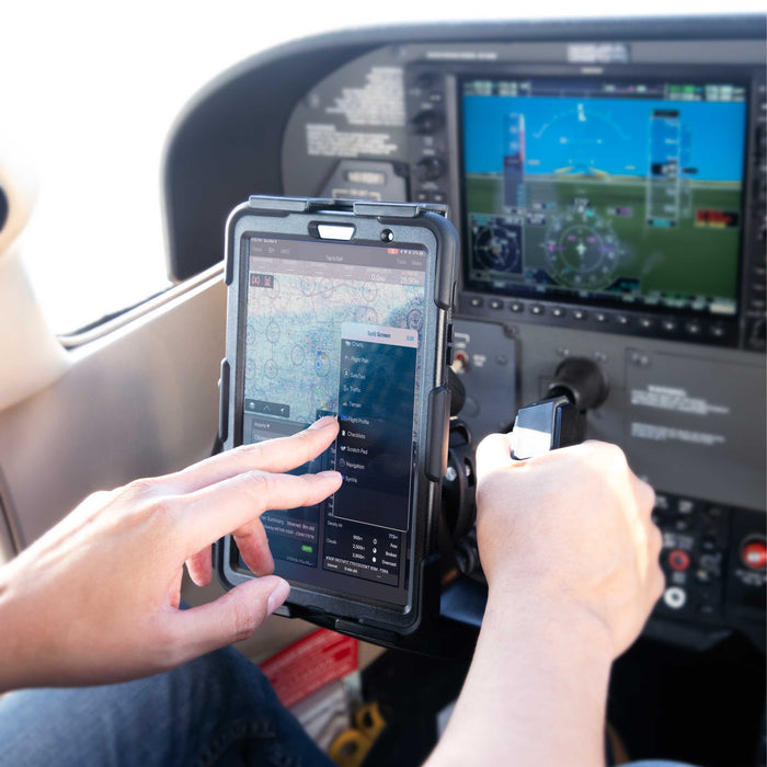 A pilot uses a tablet mounted near the controls with a SkyHold iPad Yoke Mount, navigating the screen with one hand while holding the aircraft yoke with the other. Flight display screens and navigation equipment are visible.