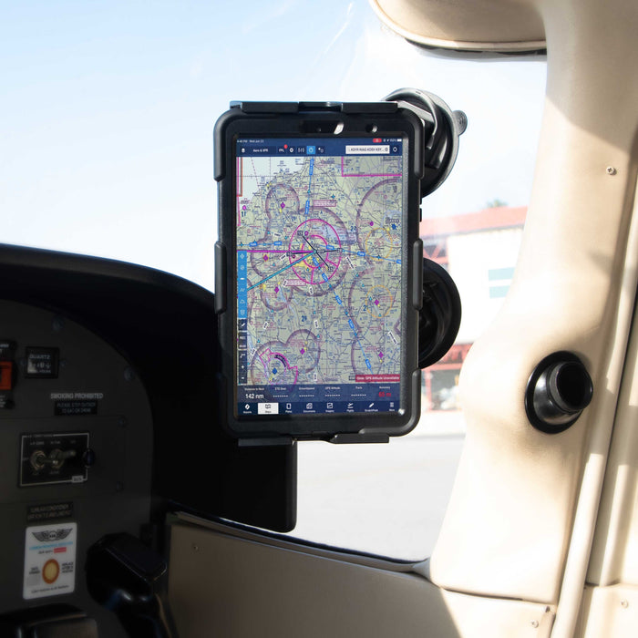 A SkyHold™ Windshield Dual Suction Tablet Mount secures a tablet showing an aviation navigation chart in the cockpit of a small aircraft, next to the control panel and window, with sunlight streaming into the interior.