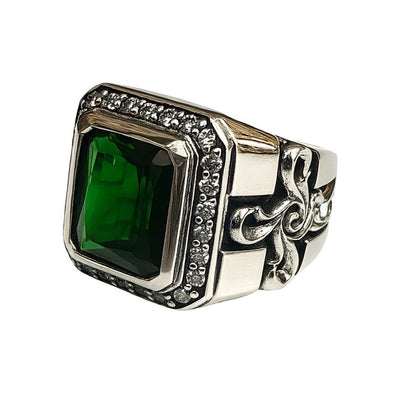 A heavy silver signet ring with a green stone and a Fleur de Lis or floral cross carved on the shank.