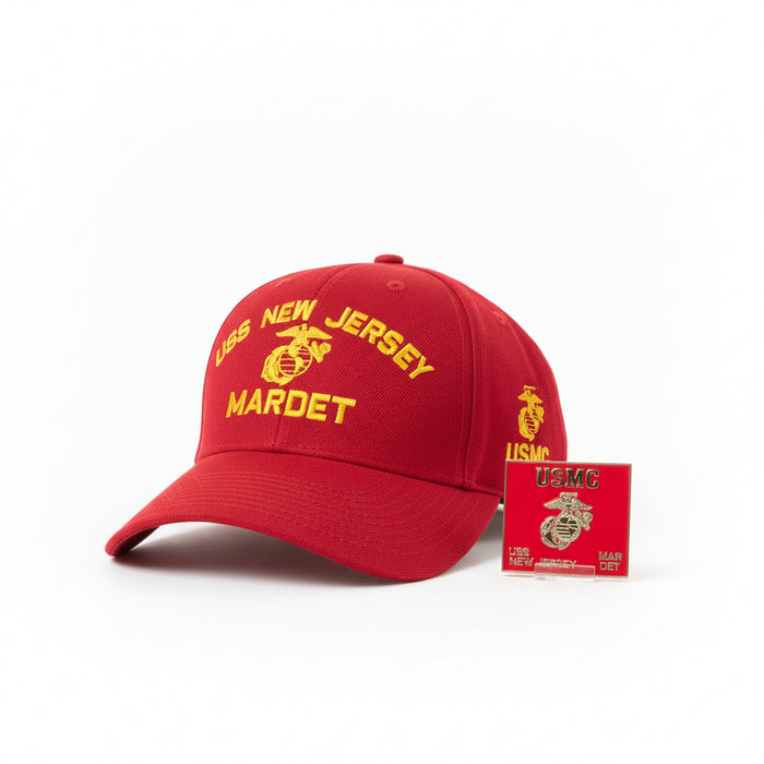 A red baseball cap with 'USMC NEW JERSEY MARDET' text in yellow, displayed in a museum setting with a framed USMC emblem on the wall and a ship's structure visible.